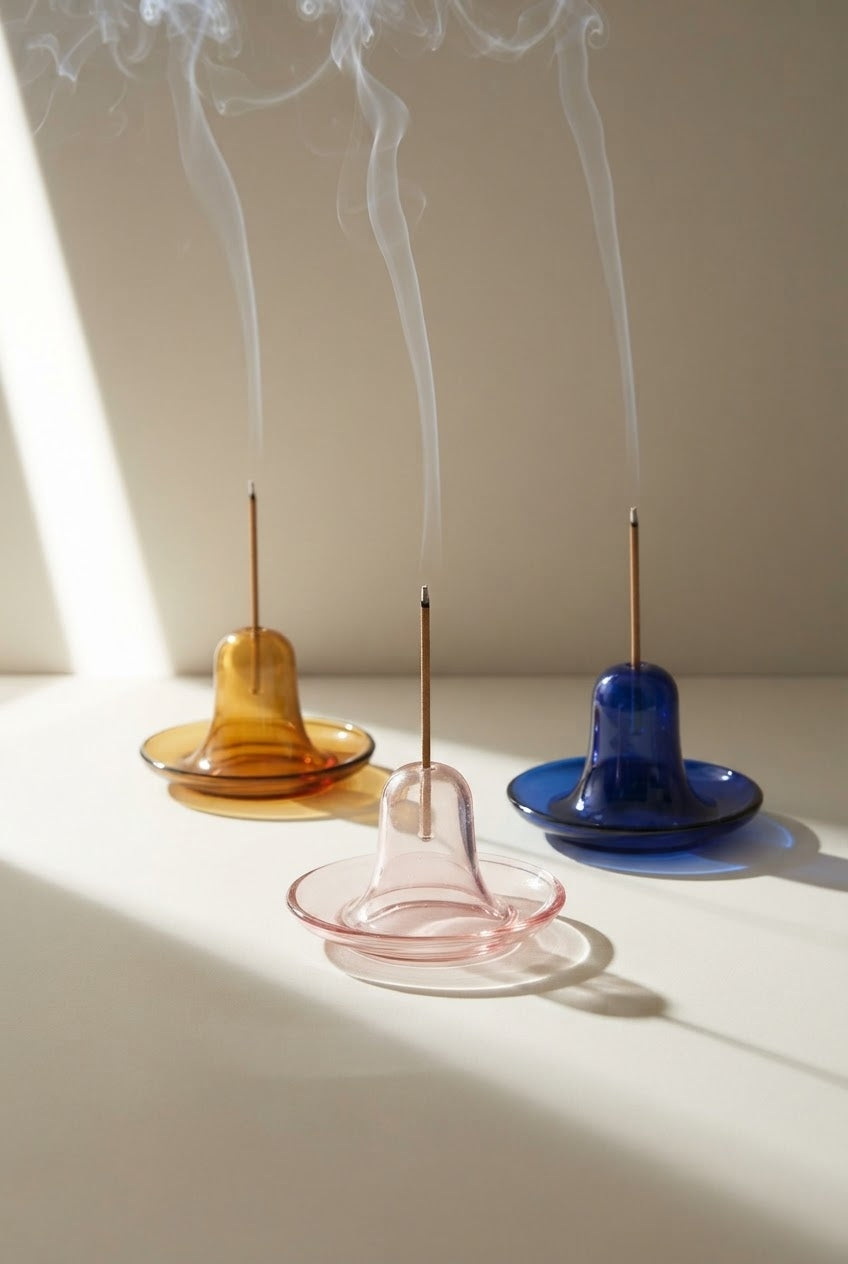 Incense holders in amber, pink, and blue glass with burning incense sticks