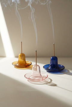 Incense holders in amber, pink, and blue glass with burning incense sticks